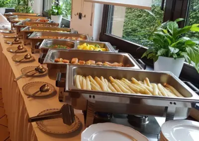 Ein Buffet mit verschiedenen Speisen, darunter Spargel, in Edelstahlbehältern auf einem Tisch.